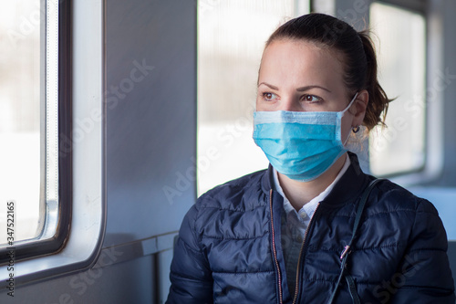 Young serious woman wearing medical protective mask on her face against coronavirus, beautiful girl sitting alone in train, public transport. Corona virus, pandemic, Covid-19, health, travel concept
