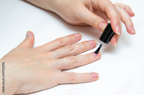 Manicure at home  during quarantine. Home manicure. The girl applies a transparent varnish  cuticle oil  nails on a white background with a brush on the nail.  Macro