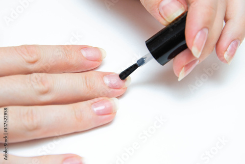 Manicure at home  during quarantine. Home manicure. The girl applies a transparent varnish  cuticle oil  nails on a white background with a brush on the nail.  Macro