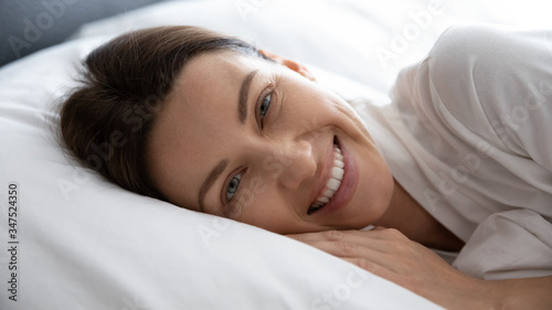 Close up woman face smiling awakened lying feels rested, enjoying comfortable bed ergonomic pillow, fresh sheets breathable soft bed clothes orthopaedic mattress, comfy quality night sleeping concept