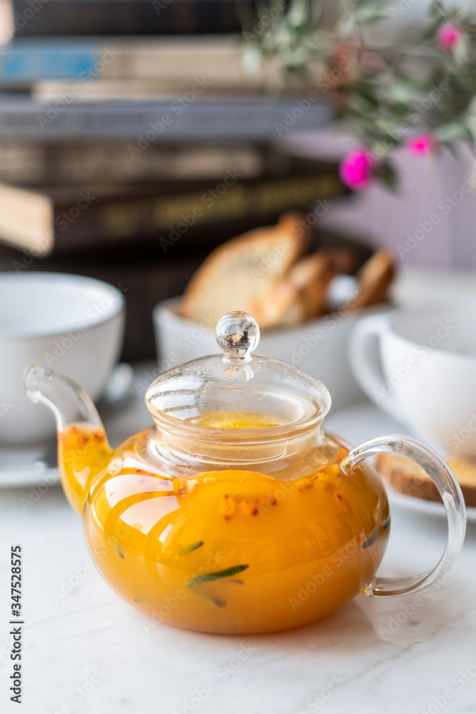 Sea-buckthorn tea in a glass teapot with white mugs on a light background. selective focus. Sea-buckthorn tea in a glass teapot with white mugs on a light background. selective focus.