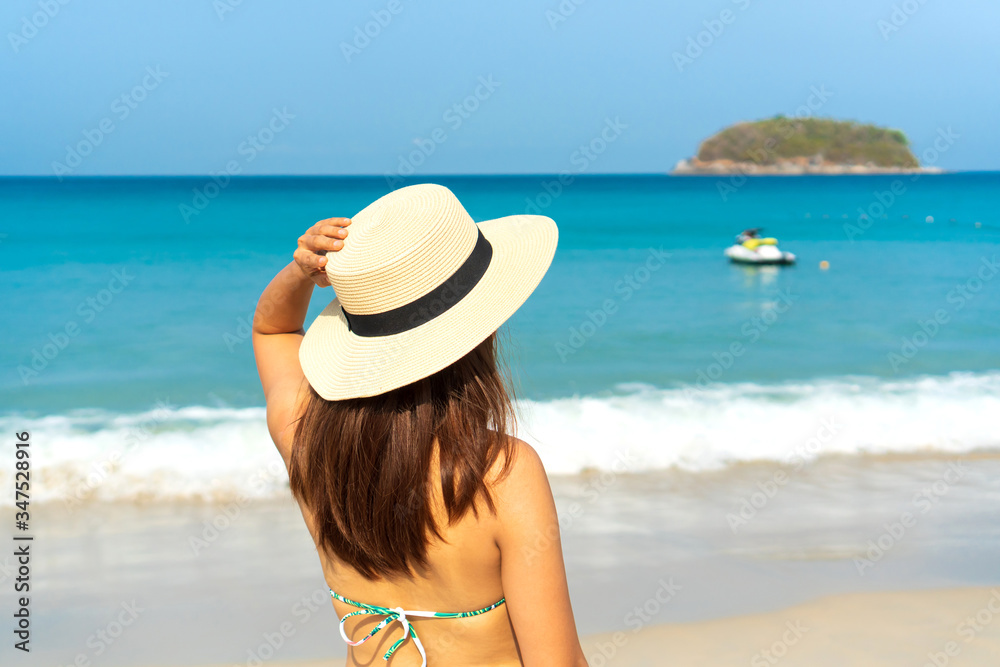Happy traveller Asian woman in bikini with beach hat enjoys at tropical beach on vacation. Summer on beach concept.