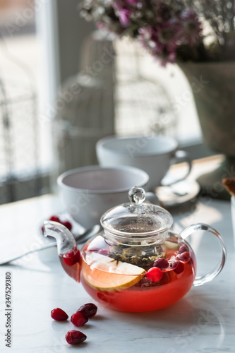 hot fruit tea with cranberries and apples in a glass teapot on a light background. selective focus.