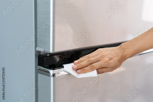 Hands of young Asian woman cleaning stainless steel refrigerator with wet wipe tissue at home