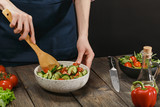 Woman mixing fresh healthy vegetable salad on wooden table. Female hands with copyspace.