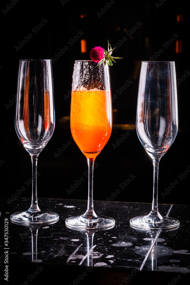 Composition with tall glass cocktail glass with orange cold drink, ice cubes melting on a dark shiny surface on a deep black background