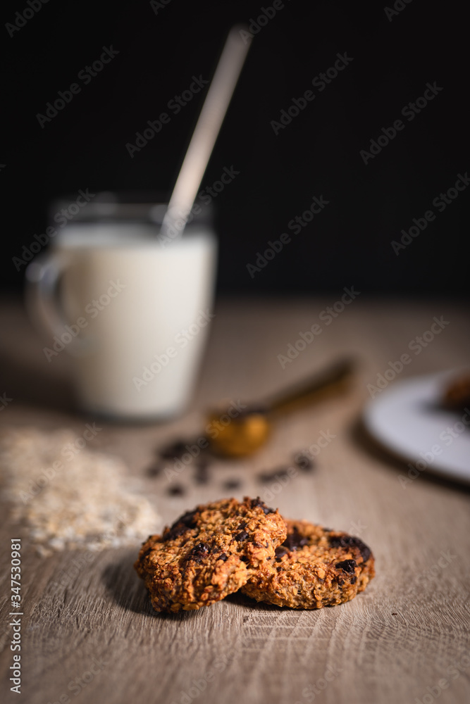 Oat chocolate cookies close up with a cup of milk, rolled oats and chocolate cookies Oat chocolate cookies close up with a cup of milk, rolled oats and chocolate cookies