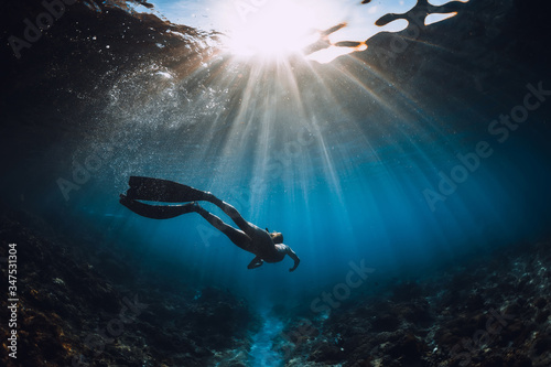 Free diver woman with fins glides over coral bottom and amazing sun rays. Freediving underwater in sea © artifirsov