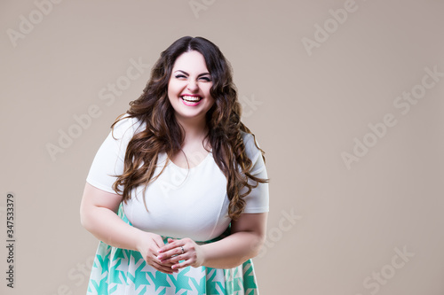 Laughing happy plus size model in casual clothes, fat woman on beige background