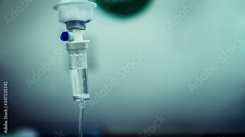 Cinemagraph of a fluid intravenous saline drip in a hospital room. Close up on Set IV fluid intravenous drop saline on a dark blue light background. Loop, selective focus, and copy space.