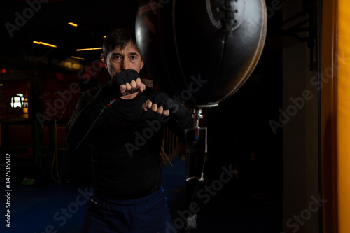 A mature male boxer in the gym. Training punches on a small punching bag. Professional trainer.