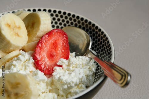 Cottage cheese, banana, strawberries and a spoon in a plate