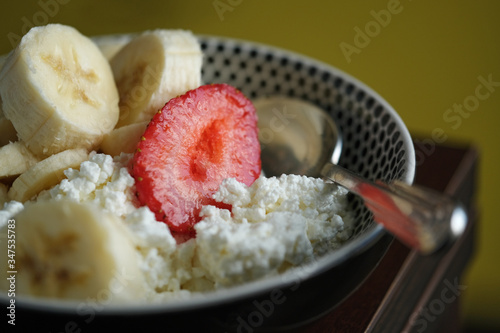 Cottage cheese, banana, strawberries and a spoon in a plate