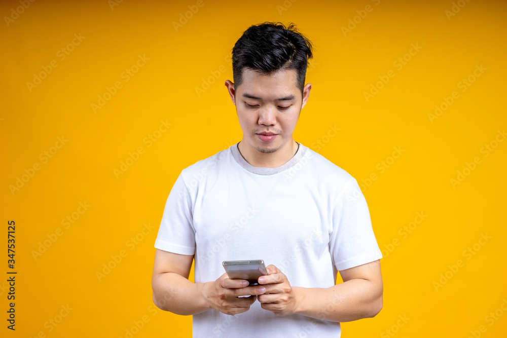 Portrait Asian young man looking at mobile phone isolated over yellow background. Portrait Asian young man looking at mobile phone isolated over yellow background.