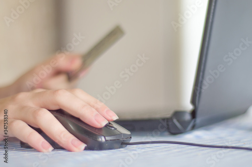 female hand holding black mouse, using notebook at home and in the other hand holding a credit card, online shopping concept