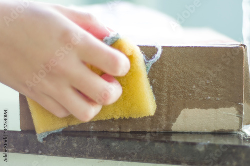 female hand disinfecting order received in cardboard box with cleaning sponge, yellow and green, cleaning to protect against viruses and bacteria