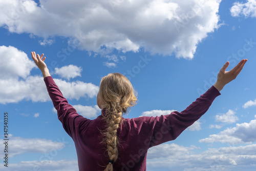 Back view. Portrait of a woman stretching her arms outdoors towards the sky.