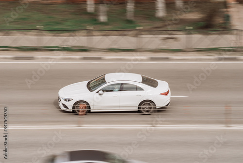 Side view rolling shot with white car in motion. Vehicle driving along the street in city with blurred background. Car driving fast on highway motion blur