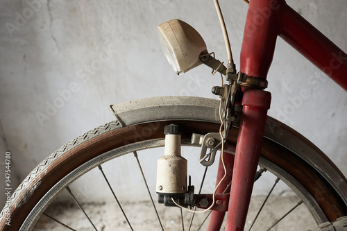 A wheel of a vintage bicycle with a dynamo and headlight in white background