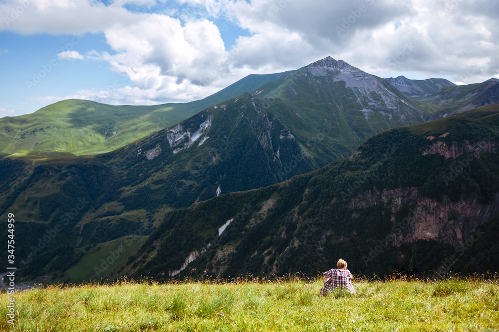 Traveler hiking alone young man sits on a green meadow in front of a mountain landscape. Summer time. Travel. Georgia. adventure, active, lifestyle, vacations, outdoor