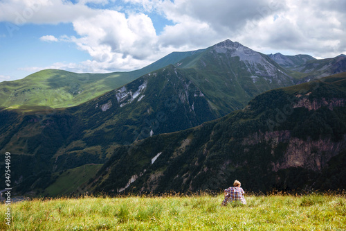Traveler hiking alone young man sits on a green meadow in front of a mountain landscape. Summer time. Travel. Georgia. adventure, active, lifestyle, vacations, outdoor © Amina