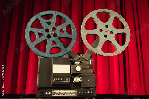 Old movie projector in the cinema with red velvet curtain in the background