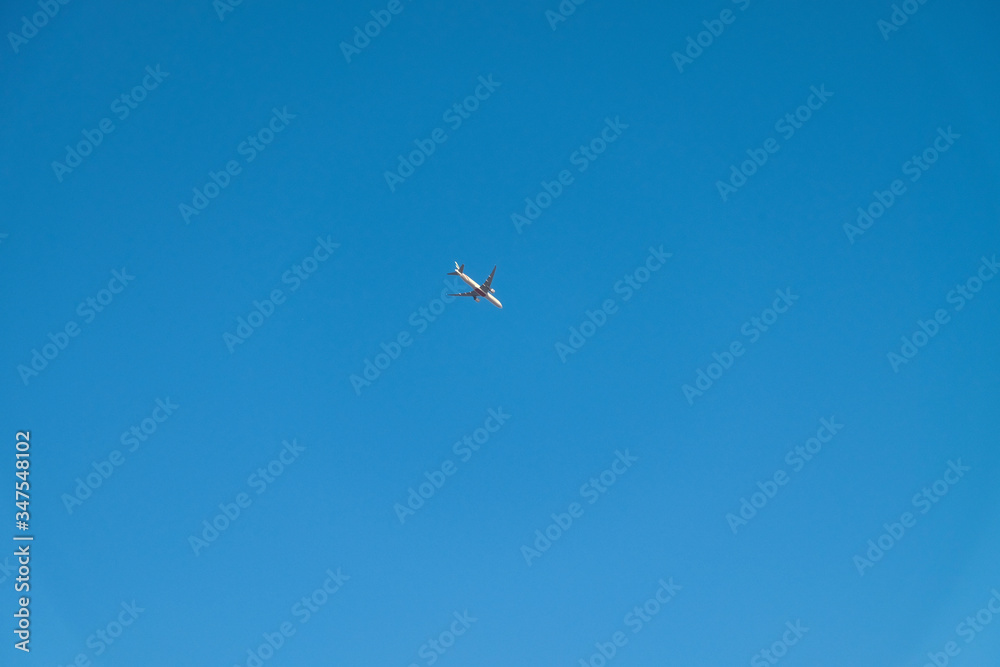 A small plane flies high in a blue sky without clouds. Airplane on a blue natural background. Background color with gradient and grain, sound effect.