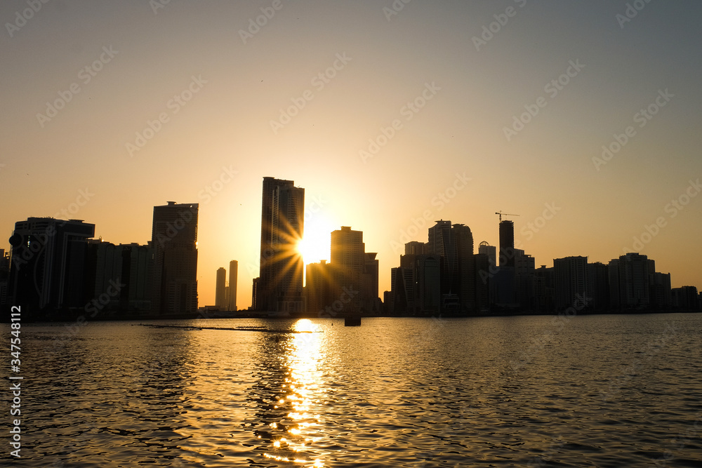 Sunset in the UAE Emirate of Sharjah-View of the river and skyscrapers. Sunset through the building. Sunset in the UAE Emirate of Sharjah-View of the river and skyscrapers. Sunset through the building.