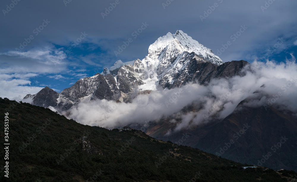 Thamsherku Mountain peak shining with sunlight above a band of clouds. A beautiful scenery of high-altitude alpine forest, mountain peak and nature in Sagarmatha National Park in Nepal. 