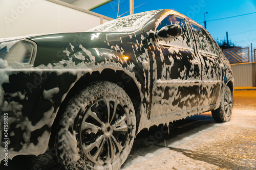 The car is covered with white washing foam. Car wash photo