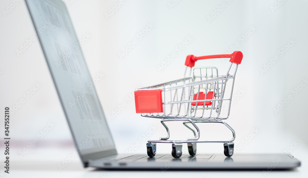 Red trolley on laptop keyboard.A cart and notebook computer on white background.Electronic commerce that allows consumers to directly buy goods from a seller over the internet.Shopping online concept.