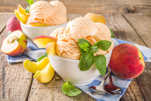 Homemade sweet peach ice cream. Peach gelato balls in small bowls, on wooden background with fresh peaches and mint leaves photo