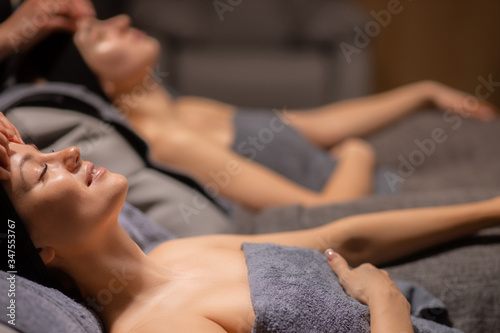 two attractive women are pampered themselves at the health spa, get face lift massage in wellbeing salon. professional beauticians make anti aging massage on neck and face