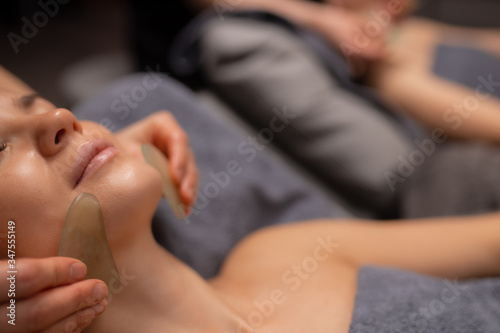 young beautiful woman get face lift massage with the use of Quartz Gua Sha Massage Tool  in luxury spa salon. close-up photo
