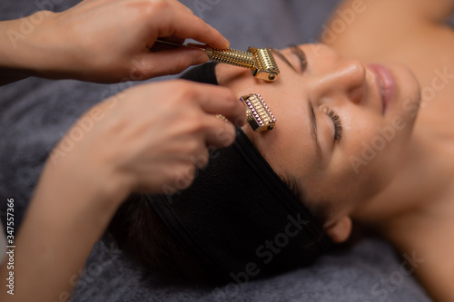 masseur use jade roller for facelift, cosmetologist drives tool on forehead for getting smooth skin