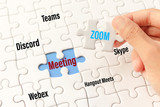 Bangkok, Thailand - May 10, 2020 : Hand holding zoom word on white jigsaw puzzle is connect to meeting word on blue gap - idea match (Teams, Discord, webex, Hangout Meets, skype) concept.