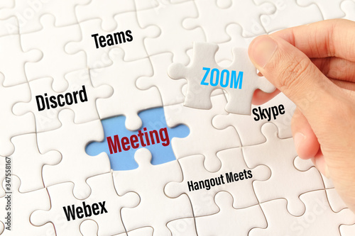 Bangkok, Thailand - May 10, 2020 : Hand holding zoom word on white jigsaw puzzle is connect to meeting word on blue gap - idea match (Teams, Discord, webex, Hangout Meets, skype) concept.