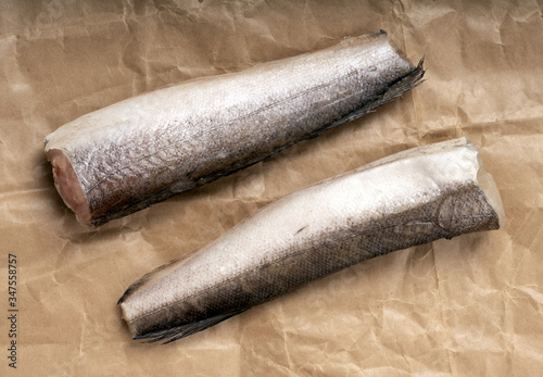 Two frozen hake, headless and tailless fish, on rough brown crumpled paper. photo