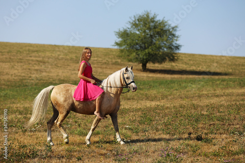 Lonely gorl on ponny without saddle on meadow in summer sunny afternoon photo