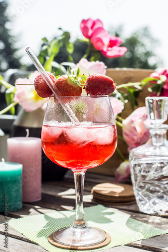 Strawberry Cocktail on a wooden table in the sun with flowers and candles