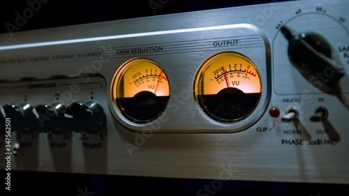 Cinemagraph of an analog VU meter moves in sync with sound level. Close up on sound mixer equalizer console with many buttons at a recording studio. Loop with selective focus.