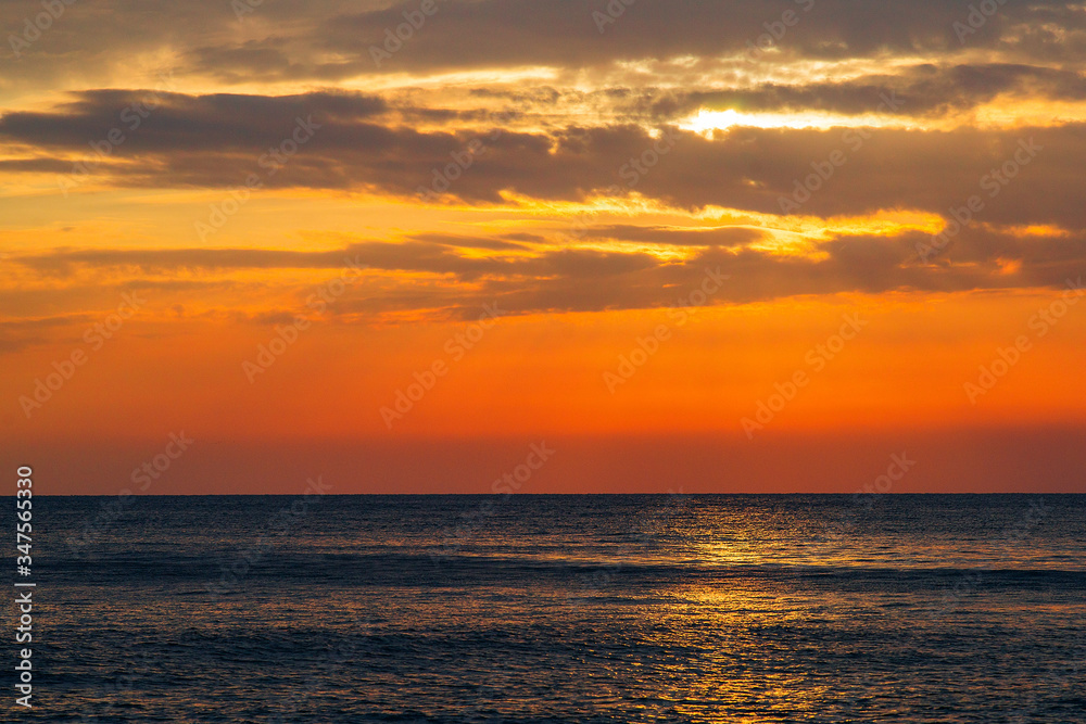 Beautiful sunset on the sea. The rays of the setting sun Shine through the clouds in the orange sunset sky. A luminous path from the sun on the sea surface.