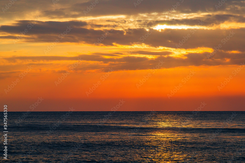 Beautiful sunset on the sea. The rays of the setting sun Shine through the clouds in the orange sunset sky. A luminous path from the sun on the sea surface. Beautiful sunset on the sea. The rays of the setting sun Shine through the clouds in the orange sunset sky. A luminous path from the sun on the sea surface.