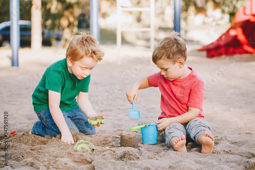 Two Caucasian children sitting in sandbox playing with beach toys. Little boys friends having fun together on a playground. Summer outdoor activity for kids. Leisure time lifestyle childhood. photo