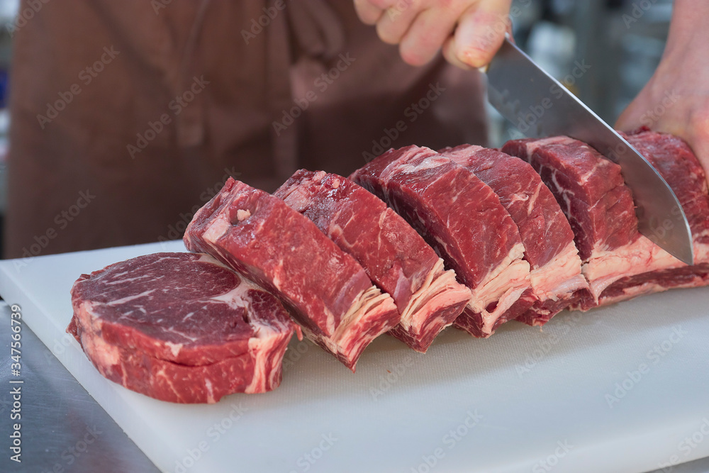 Obraz premium Butcher cutting beef in the kitchen. Closeup of hands with a knife and meat.