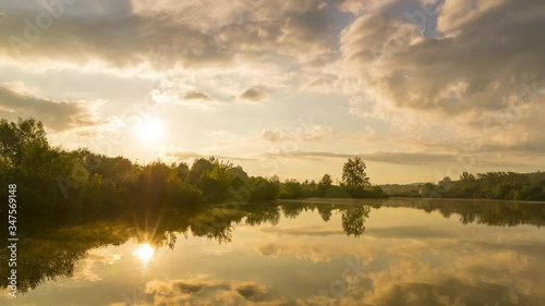 Timelapse of sunrise over lake where the sun rises behind a line of stoma on the shore and gradually changes orange color to daylight with reflection on water surface Hustopece Becvou Czech Republic