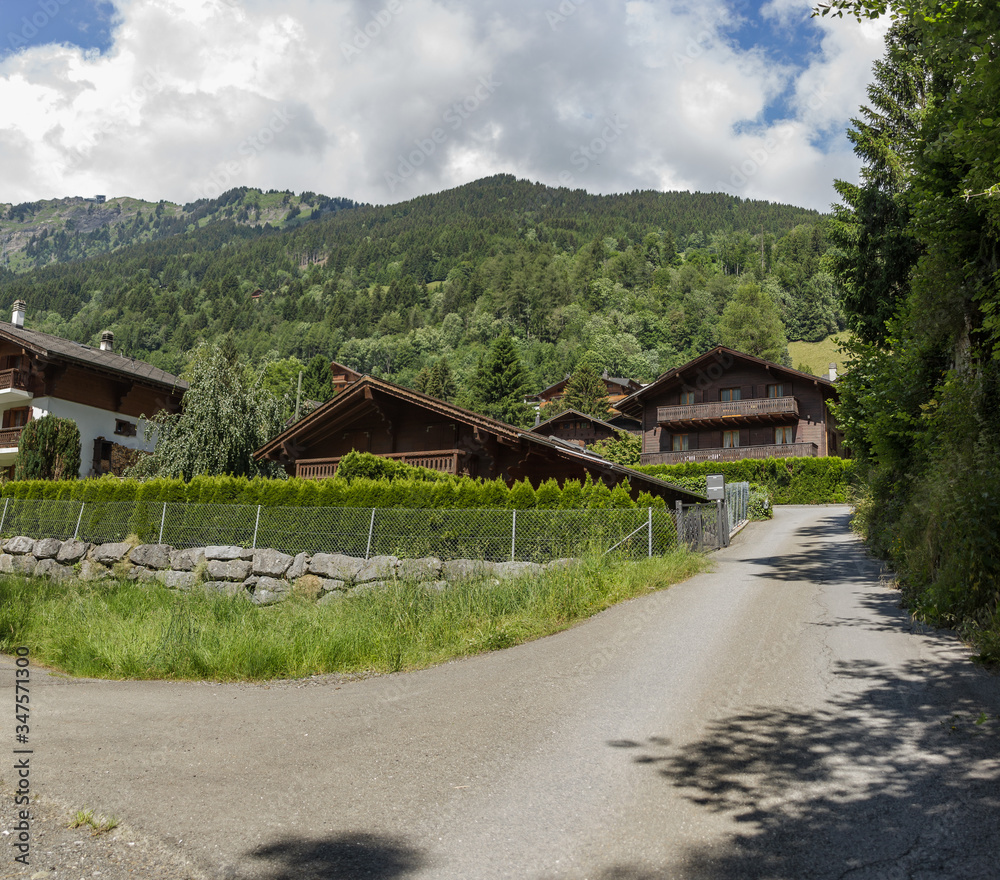 Classic swiss chalets along rustic local road. Cozy rural village Champery in Switzerland. Bright blue sky and white fluffy clouds over rocky peaks Classic swiss chalets along rustic local road. Cozy rural village Champery in Switzerland. Bright blue sky and white fluffy clouds over rocky peaks