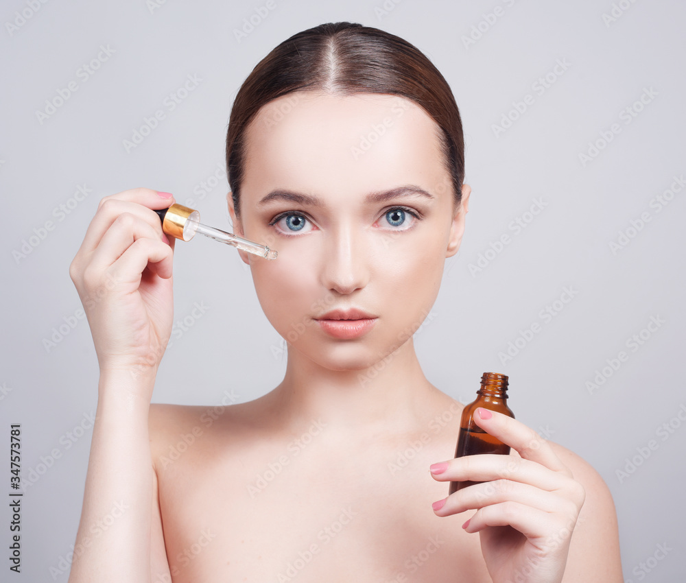 Obraz premium Close up of pretty brunette lady applying cosmetic oil on her face with pipette. Beauty therapy concept. Model with blue eyes, skin care. Organic essential oil with for beauty and spa treatment