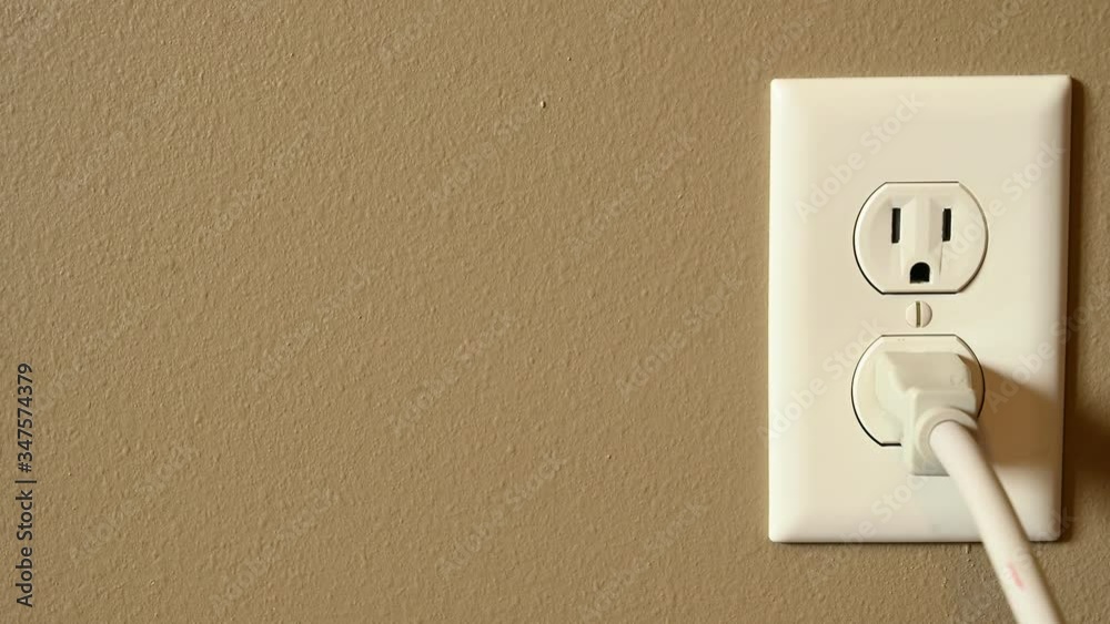 Caucasian hand gripping a three pronged power cord to insert into a power outlet