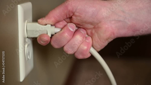 Side view of Caucasian hand gripping a three pronged power cord to insert into a power outlet